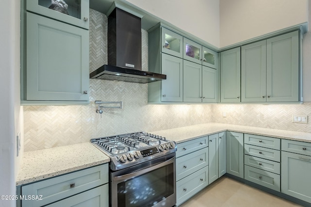 kitchen featuring decorative backsplash, wall chimney range hood, light stone counters, and stainless steel gas stove