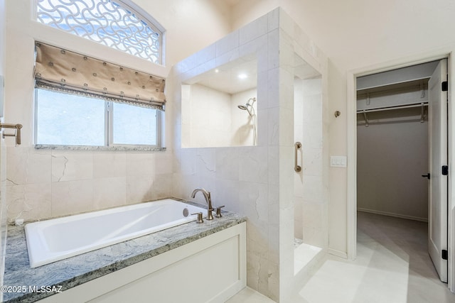 bathroom with a garden tub, a spacious closet, tile walls, and a tile shower