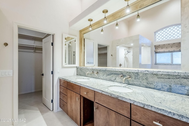 bathroom featuring a walk in closet, double vanity, a tile shower, and a sink