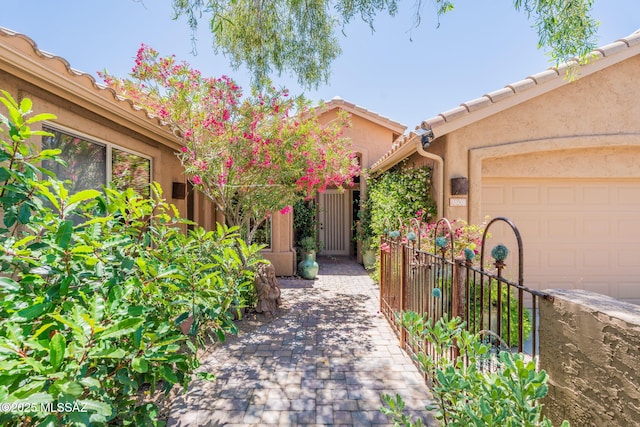 doorway to property with stucco siding, a tiled roof, a garage, and fence