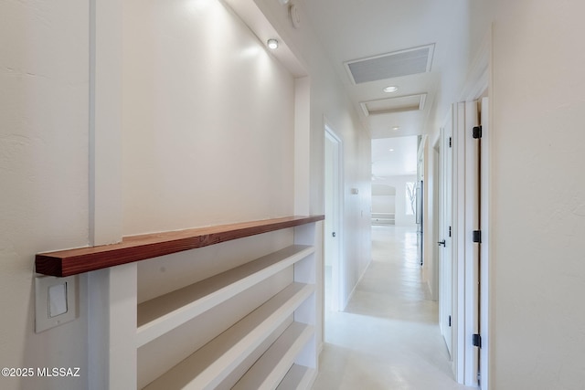 hall featuring concrete floors, visible vents, and attic access