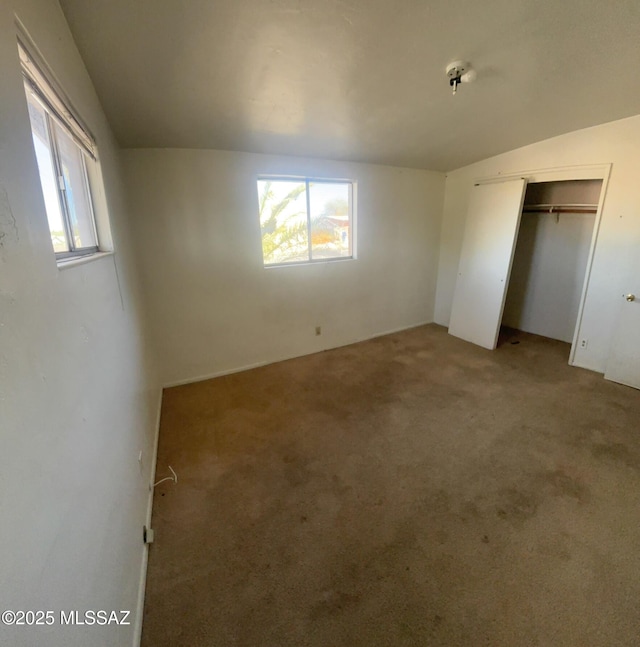 unfurnished bedroom featuring a closet, multiple windows, light carpet, and vaulted ceiling