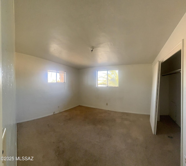 unfurnished bedroom featuring multiple windows, lofted ceiling, and carpet floors