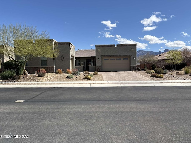 pueblo-style home with decorative driveway, a garage, and stucco siding