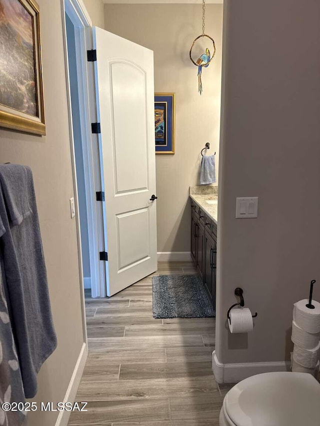 half bathroom featuring toilet, vanity, baseboards, and wood finished floors