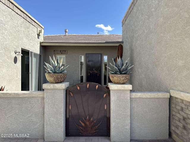 view of exterior entry with stucco siding, fence, and a gate