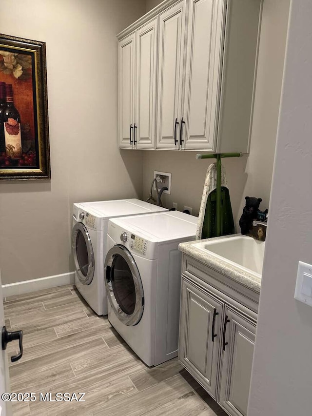 laundry area featuring baseboards, cabinet space, a sink, light wood-style floors, and washer and clothes dryer