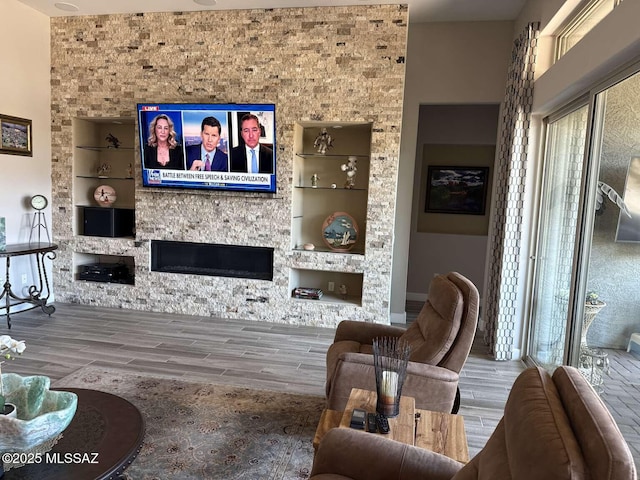 living room with built in shelves, a stone fireplace, and wood tiled floor