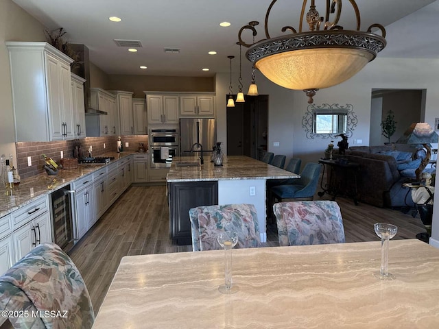 kitchen featuring wood finished floors, light stone countertops, beverage cooler, appliances with stainless steel finishes, and backsplash