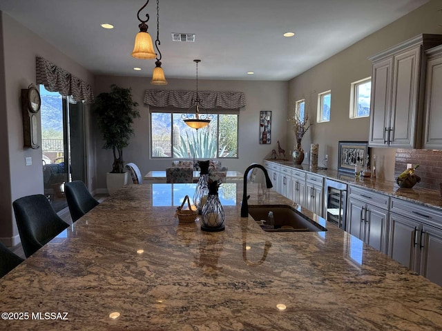 kitchen featuring a healthy amount of sunlight, beverage cooler, visible vents, stone countertops, and a sink