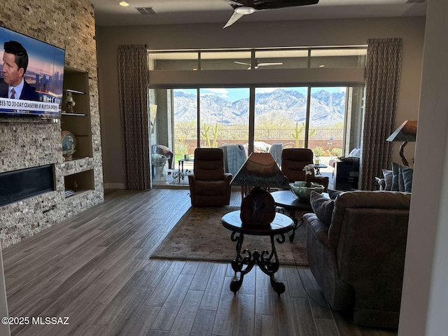 living area with a stone fireplace, wood finished floors, visible vents, and a healthy amount of sunlight