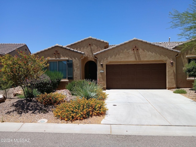 mediterranean / spanish-style home featuring a tiled roof, an attached garage, driveway, and stucco siding