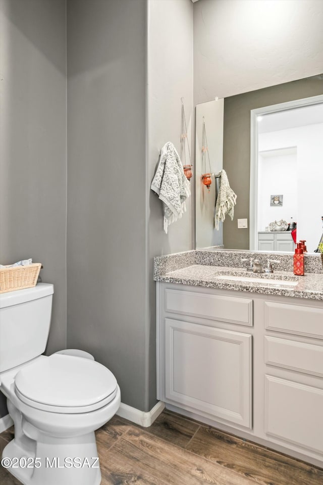 half bathroom with vanity, toilet, wood finished floors, and baseboards