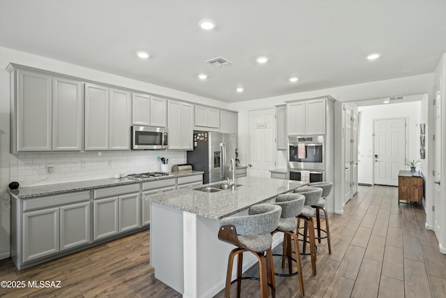 kitchen featuring visible vents, gray cabinetry, a sink, tasteful backsplash, and appliances with stainless steel finishes