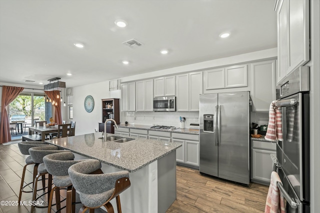 kitchen featuring visible vents, a sink, tasteful backsplash, appliances with stainless steel finishes, and light stone countertops