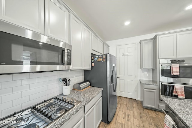 kitchen with light stone counters, tasteful backsplash, appliances with stainless steel finishes, and light wood-style flooring