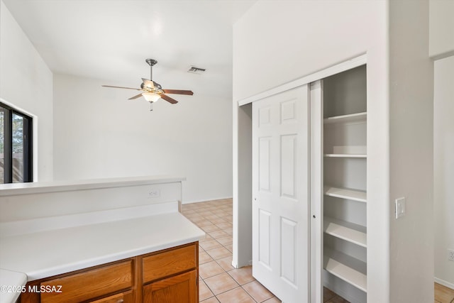 kitchen featuring visible vents, a ceiling fan, brown cabinetry, light countertops, and light tile patterned floors