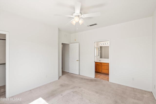 unfurnished bedroom with visible vents, light carpet, connected bathroom, baseboards, and ceiling fan