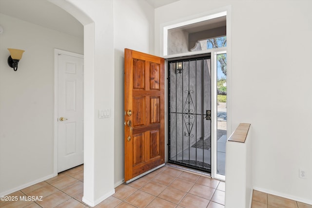 foyer entrance featuring light tile patterned floors, arched walkways, and baseboards