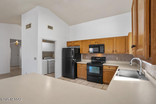 kitchen with visible vents, a sink, decorative backsplash, black appliances, and washer and dryer