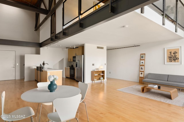 dining room featuring visible vents, light wood-style flooring, stairs, and a towering ceiling