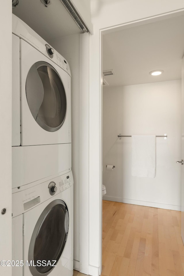 laundry area featuring stacked washer / dryer, laundry area, light wood-type flooring, and baseboards