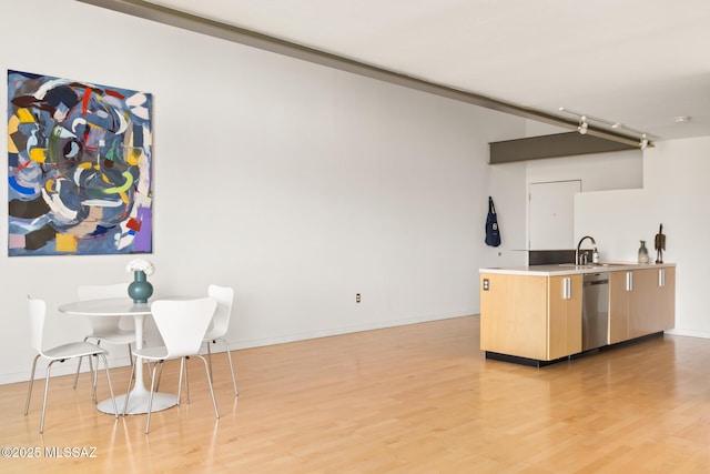 kitchen featuring light wood-style flooring, light brown cabinetry, a sink, baseboards, and dishwasher