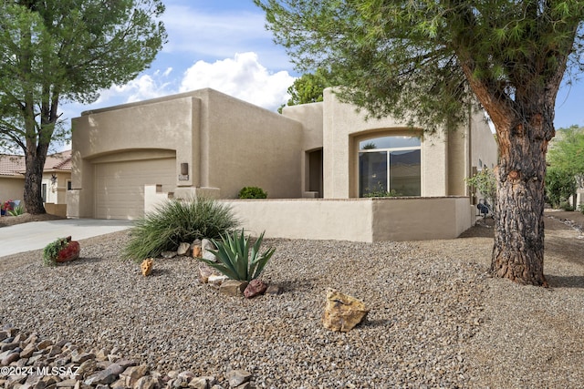 pueblo-style house featuring concrete driveway, an attached garage, and stucco siding