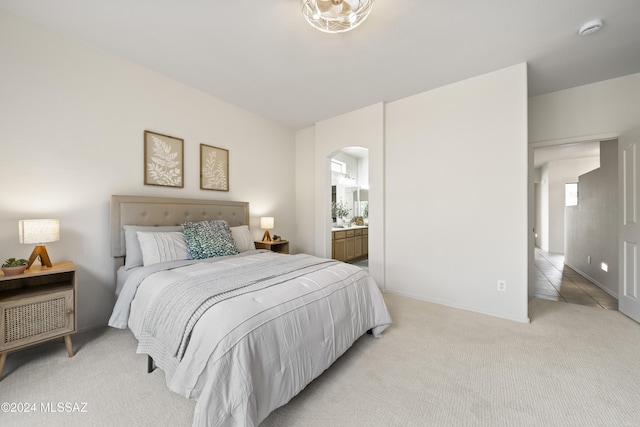 bedroom with light carpet, arched walkways, and ensuite bathroom