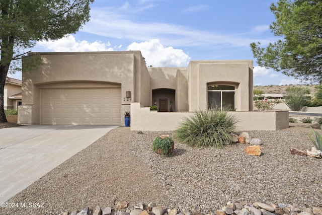 pueblo-style home featuring a garage, driveway, and stucco siding