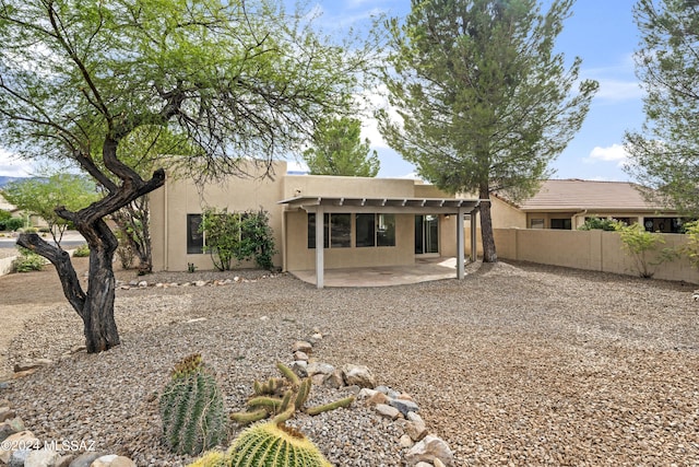 rear view of property featuring a patio area, fence, and stucco siding