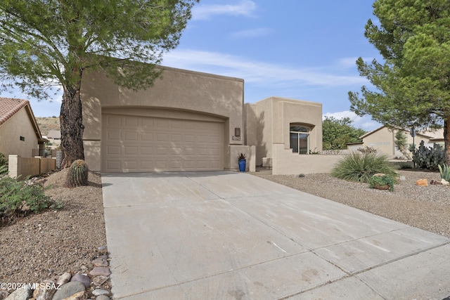 pueblo revival-style home with concrete driveway, an attached garage, fence, and stucco siding