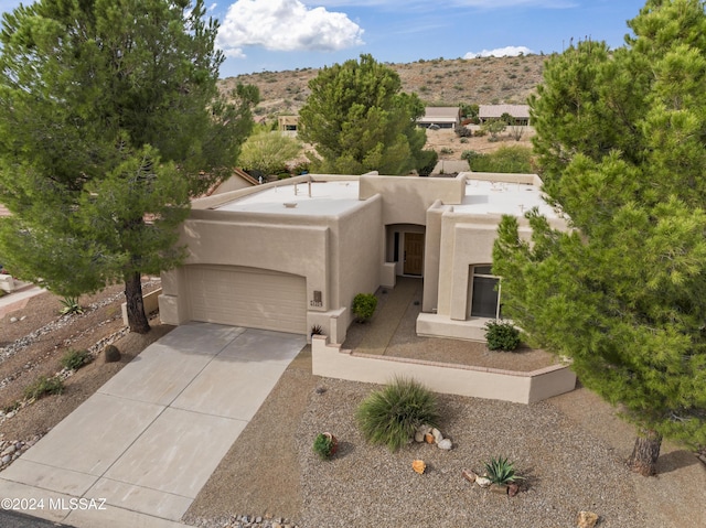 pueblo-style home featuring concrete driveway, stucco siding, a mountain view, and an attached garage