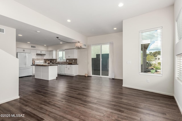 unfurnished living room with dark wood-style floors, visible vents, baseboards, recessed lighting, and a notable chandelier