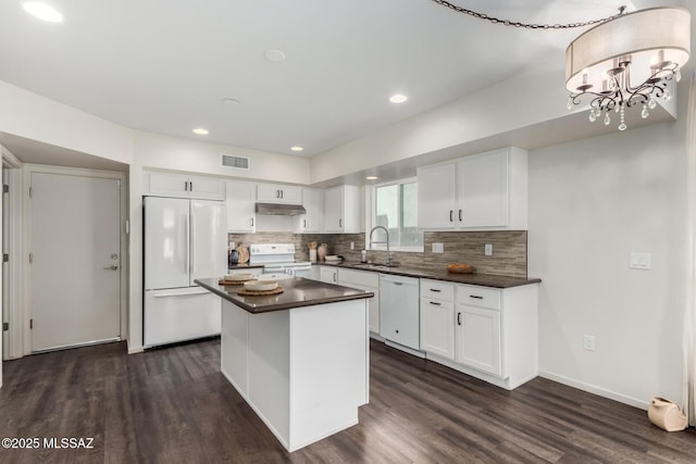 kitchen with visible vents, a sink, dark countertops, dark wood-style floors, and white appliances