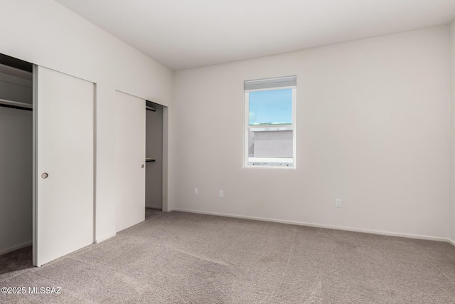 unfurnished bedroom with multiple closets and light carpet