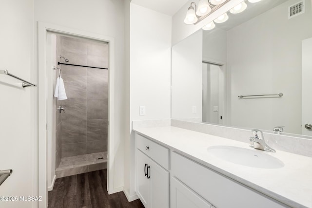 bathroom featuring vanity, wood finished floors, visible vents, and a tile shower