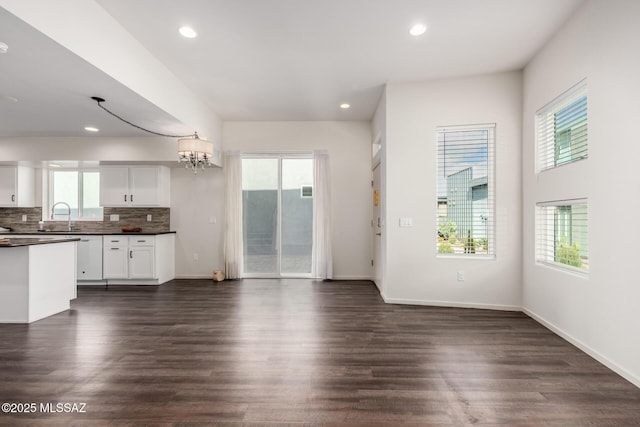 kitchen with a sink, backsplash, dark countertops, dark wood-style floors, and a chandelier