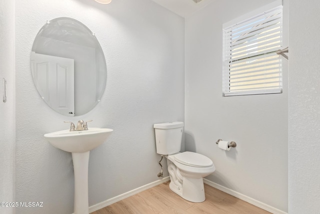 bathroom featuring toilet, wood finished floors, baseboards, and a sink