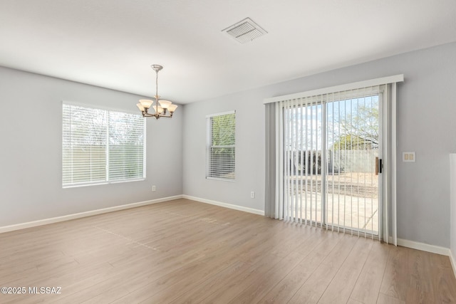 spare room with baseboards, visible vents, light wood finished floors, and a chandelier