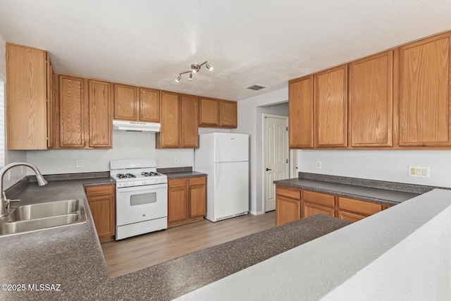 kitchen with under cabinet range hood, white appliances, dark countertops, and a sink