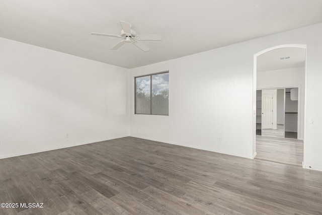 unfurnished room with visible vents, baseboards, wood finished floors, arched walkways, and a ceiling fan