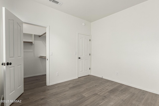 unfurnished bedroom featuring a walk in closet, wood finished floors, visible vents, and baseboards