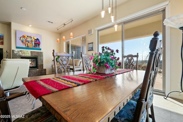 tiled dining room featuring rail lighting, visible vents, and a high end fireplace