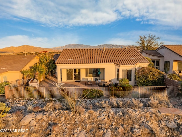 back of house with a tiled roof, a fenced backyard, a mountain view, and stucco siding