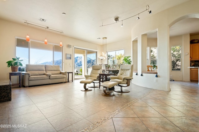 interior space featuring light tile patterned floors, visible vents, baseboards, arched walkways, and track lighting