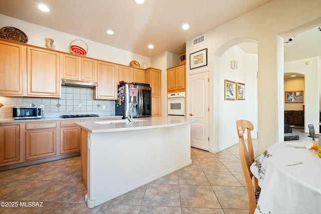 kitchen with backsplash, under cabinet range hood, light countertops, arched walkways, and stainless steel appliances