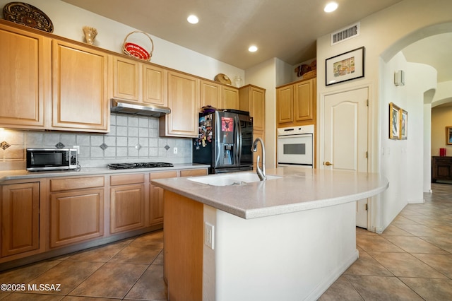 kitchen featuring gas cooktop, arched walkways, under cabinet range hood, white oven, and refrigerator with ice dispenser