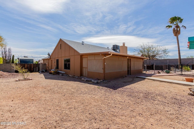 rear view of property featuring a chimney, fence, and central AC