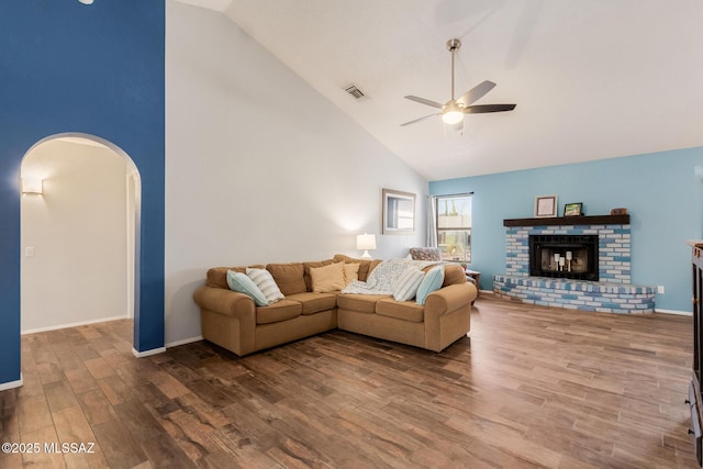 living room featuring a fireplace, visible vents, ceiling fan, arched walkways, and wood finished floors